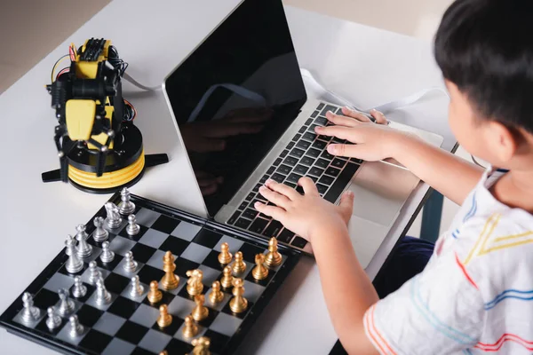 Asian little boy programming code to robot machine arm on laptop for play chess, STEM education E-learning, Funny children learning getting lesson control robot arm, Technology science education