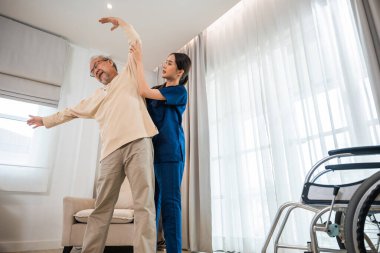 Old senior man enjoys training with physiotherapist for outstretched arms at home, Asian physical therapist patient nursing helping elderly exercising arm stretch, Rehabilitation of disabled concept