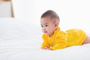 Yeni doğmuş güzel Asyalı bebeğin portresi evde yatağında yatar mutlu bebek gülüşü odada dinlenen sarı bir gömlek giyer aile sabahı evde dinlenir.