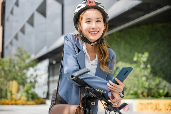 Asian smiling young woman with helmet hold mobile smart phone talk with business during go to office work at street with bicycle, Eco friendly, Lifestyle business female using bike outdoor in morning