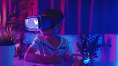 Sanal gerçeklik gözlüğü takan Asyalı küçük çocuk gerçeklik gözlüğü takıyor, çocuk VR başlığı takıyor sola bak, sağa bak ve evde heyecanlı ol koyu mor ve mavi arka plan, sanal teknoloji.