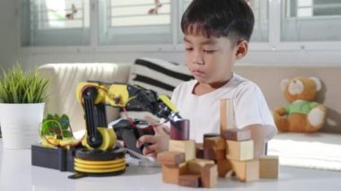 Uzaktan kumandayla tahta bloğu kaldırmak için robot kolu kullanan mutlu Asyalı çocuk, eğlenceli çocuk, başarılı bir ders kontrolü robot kolu, teknoloji bilimi eğitimi alıyor.
