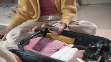 Woman using smartphone blank green screen for checklist and packing suitcase bag for travel trip weekend vacation at home, female check note purveyance or baggage on mobile phone