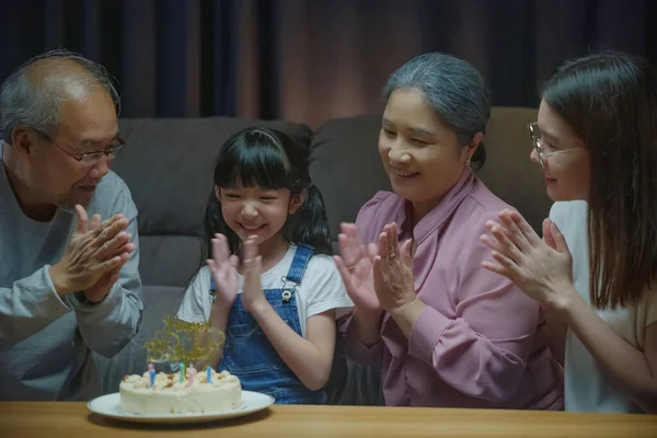 Birthday surprise. Happy Asian family grandparents and mother celebrating enjoy birthday party with cake of granddaughter at home in night time