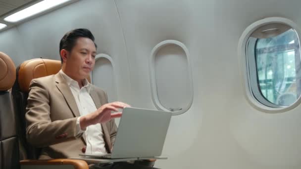 飛行機の中でノートパソコンを操作するアジア系のビジネスマン 飛行機の機内でノートパソコンを操作するビジネスマン — ストック動画