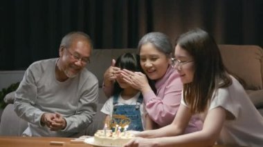 Mutlu Asyalı aile büyükbabaları ve anneleri doğum günü partisinin tadını çıkarıyor. Torunlarının pastasıyla evde mum üflüyorlar. Doğum günü sürprizi konsepti.