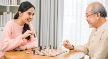 Beautiful young smile woman having fun sitting playing chess game with senior elderly at home, nurse caregiver in nursing home for leisure, Happy active retired people, Healthcare and medical concept