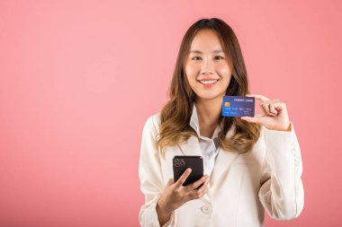 Mutlu bir Asyalı portresi güzel tatlı bir genç kadın gülümseyen cep telefonu ve plastik banka kartı, stüdyo resmi pembe arka planda, akıllı telefon kullanan bir kadın online alışveriş yapıyor.