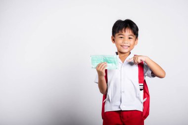 Tayland üniforması giyen Asyalı öğrenci çocuk beyaz arka planda izole edilmiş, anaokulunda izole edilmiş, okula geri dönmüş, okula gitmeden önce maskeyi korumak için işaret ediyor.