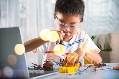 Küçük çocuk oyuncağı monte etmek için tornavidayla cevizi sıkıyor, Asyalı çocuk evde Arduino robot araba ev ödevi yapıyor, eğitim yapay zeka atölyesi dersi öğreniyor.