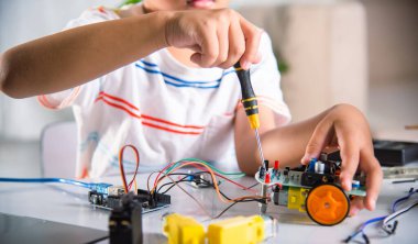 Asian kid boy assembling the Arduino robot car homework project at home, Little child tighten the nut with a screwdriver to assemble car toy, creating electronic AI technology workshop school lesson