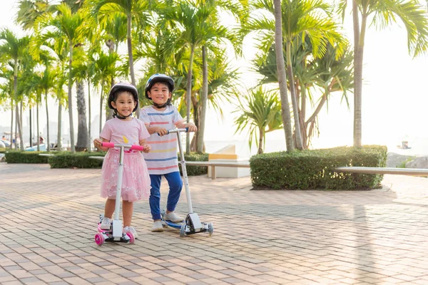 子供の乗馬スクーター 幸せなアジアの小さな子供の男の子と女の子は 夏の日に屋外の公園で道路上の安全なヘルメットプレイキックボードを着用し 外のアクティブな子供ゲーム 子供スポーツ健康的なライフスタイルの概念 — ストック写真