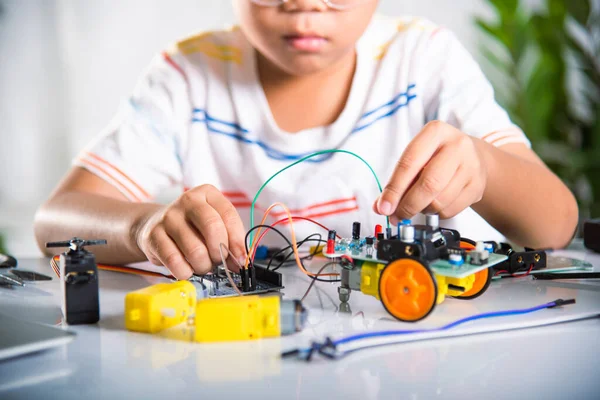 Asian kid boy plugging energy and signal cable to sensor chip with Arduino robot car, Little child remotely learn online with car toy, STEAM education AI technology course school learning lesson