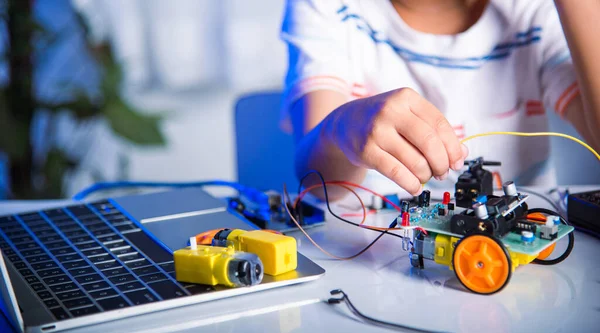 Asian kid boy plugging energy and signal cable to sensor chip with Arduino robot car, Little child remotely learn online with car toy, STEAM education AI technology course school learning lesson