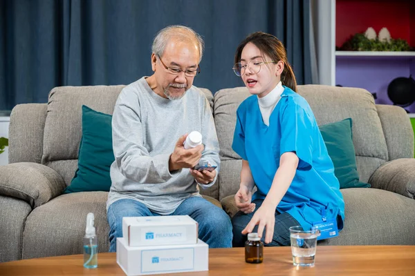 医師が処方薬を説明するアジアの看護師は 自宅で気配りのある高齢者に 医師の女性は 生活室で家の中で訪問薬の老人 医療従事者を説明します — ストック写真