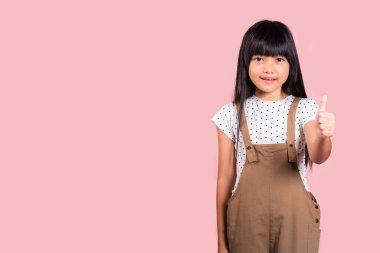 Asyalı küçük bir çocuk, 10 yaşında pembe arka planda izole edilmiş bir şekilde stüdyoda baş parmak gösteriyor mutlu çocuk portresi güzel bir jest için gülümsüyor.