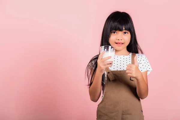 アジアの小さな子供10年古いです笑顔ホールドミルクグラスドリンクホワイトミルクとショー親指アップ指で良いサインでスタジオショットでピンクの背景に隔離されました 幸せな子供の毎日の医療医学食品 — ストック写真
