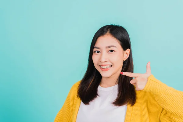 アジアの美しい若い女性ティーン指差す指に歯 幸せなタイの女性の肖像画自信を持って笑顔を示す白い歯 青の背景に隔離されたスタジオショット 歯科医療の概念 — ストック写真