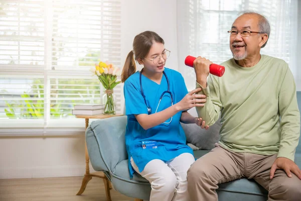 年轻的护士理疗师支持老年人在家里提起哑铃 护士用哑铃帮助老年人进行退休训练 锻炼身体康复 保健和医药 — 图库照片