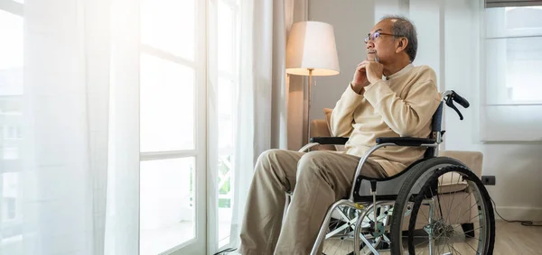 Lonely older thoughtful sad old man look outside windows in bedroom at retirement home, Asian senior man disabled feel depressed lonely sitting alone in wheelchair looking through window at hospital