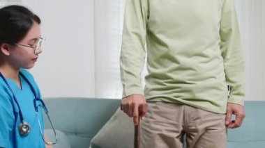 Diz ağrısı çeken yaşlı bir adamın ameliyatından sonra dizini ve bacağını kontrol eden Asyalı genç bir hemşire yaşlı bir adama bastonlu ağrı belirtilerini soruyor.