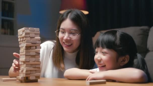 亚洲的年轻妈妈晚上和小女儿在家里客厅里玩木块游戏 微笑的女人帮助教学龄前小孩玩木块建筑塔 家里很好玩 — 图库视频影像