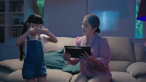 幸せなアジアの家族の祖母と孫娘は 自宅で夜にデジタルタブレットで踊り 母親は娘 シニア 子供にミルクのガラスを持ってきました — ストック動画