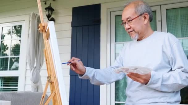 ライフスタイルの高齢者は自宅の外の彼のイーゼルで絵を笑顔 アジアの高齢者はキャンバス上のブラシとオイルの色を使用して絵を描く 幸せな退職アーティストと活動のコンセプト — ストック動画