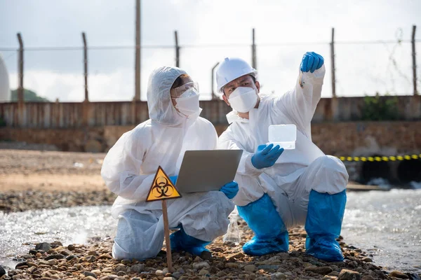 Ecologist sampling taken dead fish to inspaction and save data to laptop computer, Biologist wear protective suit and mask collects sample of waste water from industry, problem environment