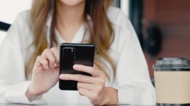 Pencerenin yanındaki kafede oturan mutlu bir kadın cep telefonu, Asyalı genç iş kadını serbest telefon ve kahve dükkanında kahve kağıdı bardağı tutuyor.