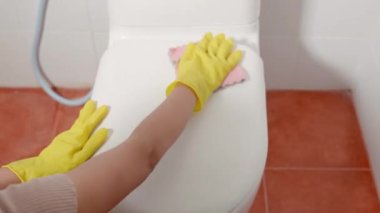 Klozet kapağını pembe bezle temizleyen kadın, sarı lastik eldiven giyen kadın oturup tuvaleti temizliyor, temizlikçi sağlık konsepti.