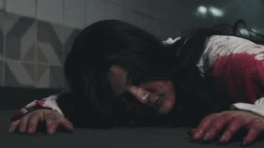 Cadılar Bayramı korku konsepti. Kan sürünen Asyalı zombi kadın yavaşça sürünüyor, ürkütücü hayalet saçlarıyla yüzünü kanla kaplıyor ve geceleri elini uzatıyor.