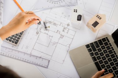 Mimari proje işyeri. Mimarlık bürosundaki masa başındaki plan taslağında pusula ile düzenlemeden ya da taslak çizmeden önce evin tasarımını gözden geçirmek için dizüstü bilgisayarın klavyesini yazmayı seç
