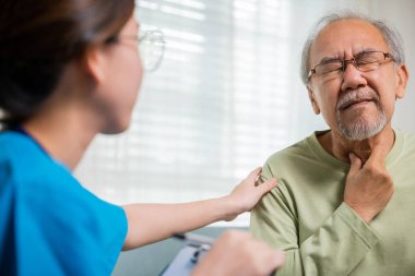 Doktor kadın, yaşlıların boynundaki lenf bezlerini şişmiş mi, boğazı ağrıyan mı, yaşlılar kliniğindeki yaşlı adamın boyun ağrısını kontrol eden Asyalı bir hemşire mi, yoksa fizyoterapist mi olduğunu anlamak için inceliyor.
