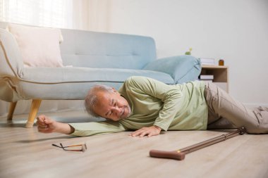 Asian old man lying on floor after falling down with wooden walking stick, Sick senior man beside couch on rug in living room at home, Elderly having an accident after doing physical therapy alone clipart