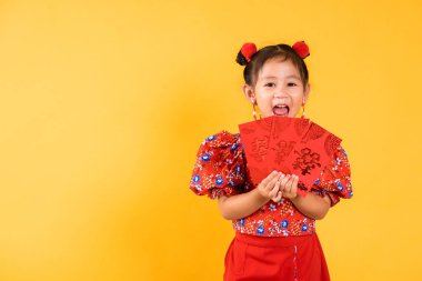 Çin Yeni Yılı. Mutlu Asyalı küçük kız gülümsemesi kırmızı cheongsam qipao tutun angpao kırmızı paket parasal hediye geleneksel elbise içinde portre çocuk, kısa sarı arka plan izole stüdyo