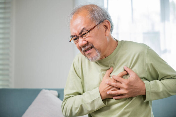 Старший мужчина плохо рука боли касаясь груди с сердечным приступом, азиатский пожилой человек имеют врожденные заболевания страдают от душевной боли в одиночестве дома его сердце болит, пожилой пенсионного здоровья заболеваний