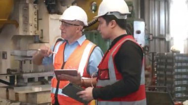 Mühendis çırağına metal levha damgalama makinesi kullanmayı öğretiyor. Endüstriyel ekip tablet bilgisayarlı çeşitli projeler üzerinde çalışıyor. İşçiler fabrikadaki işletim sistemini kontrol etmek için birlikte çalışıyorlar.
