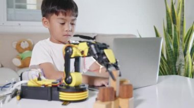 Asian little kid boy using laptop computer check on robotic arm machine in workshop, Child learning lesson programer to programming control robot arm pick up wood block, Technology science education