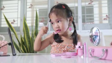 Makyaj yapan Asyalı komik küçük kız akıllı telefona bakıyor ve maskara kullanıyor, kadın olmak için öğrenme aktivitesi, sosyal medya blogcusu kozmetik ile video kaydı, online özel ders.