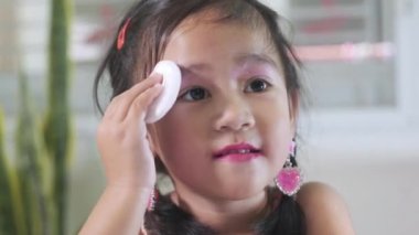 Yüzüne makyaj yapan Asyalı sevimli küçük kız yanaklarına puf puf böreği yapıyor, kadın olmak için aktivite öğreniyor, mutlu yüzlü çocuk güzel bir makyaj oyuncağı.