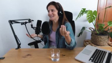 Olgun bir kadın, stüdyosundaki mikrofon ve dizüstü bilgisayarla podcast yapıyor.