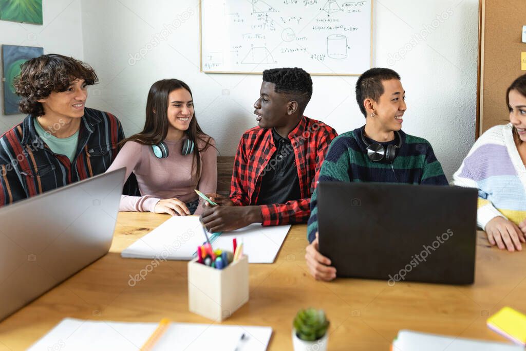 Young multiracial students reading books and using laptop in classroom while studying together - School education concept