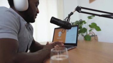 Afrikalı bir adam kendi stüdyosundan mikrofon ve laptop kullanarak bir podcast kaydediyor.