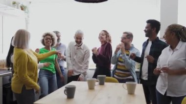Farklı yaşlarda ve etnik kökenli mutlu insanlar evde bir fincan kahve içerken dans ederek eğleniyorlar.