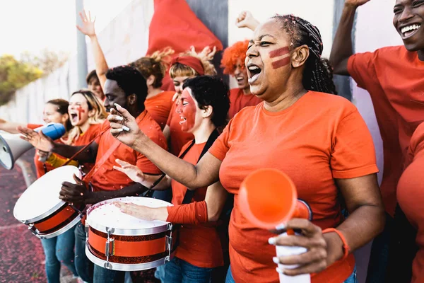 Crowd football fans exulting while watching soccer game at stadium - People with painted face and drum encouraging their team - Sport entertainment concept