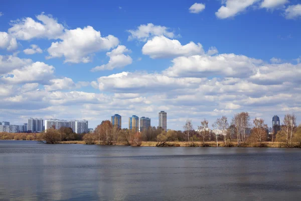 Een lente verbazingwekkend cityscape aan de rivieroever in de verte onder de blauwe hemel met mooie witte wolken. — Stockfoto