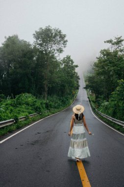 Nan, Thiland- Ekim 2021 - 1715 gökyüzü yolunun arka planındaki sisli dünyaya yağmurlu mevsimde sis dolu güzel bir kadın yürür..
