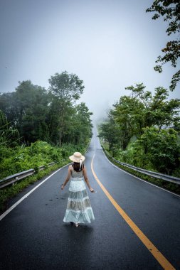 Nan, Thiland- Ekim 2021 - 1715 gökyüzü yolunun arka planındaki sisli dünyaya yağmurlu mevsimde sis dolu güzel bir kadın yürür..