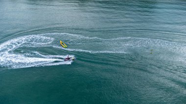 Sichon plajı, Tayland - Kasım 2021: Havadan kuş bakışı: Açık deniz turkuazında yüksek hızda seyreden tanımlanamayan muz teknesinin tanımlanamayan jet ski görüntüsü.